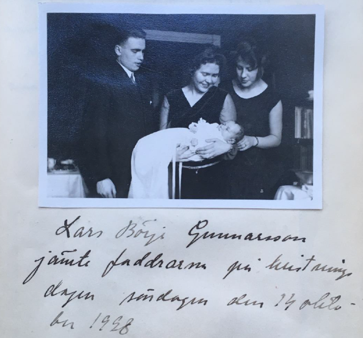 En kvinna håller ett dopklätt barn i famnen. Runt henne står en man och en kvinna, alla tittar på barnet.