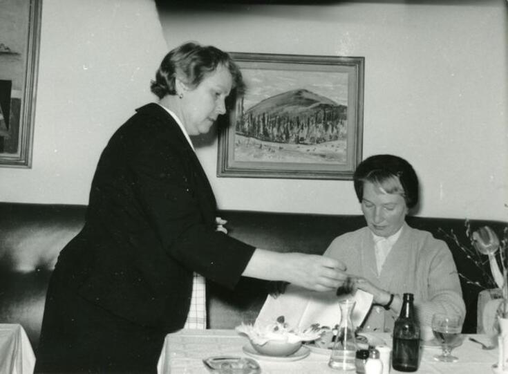 Servitris och kund på Elite. Kunden sitter vid bordet, servitrisen håller på att servera.