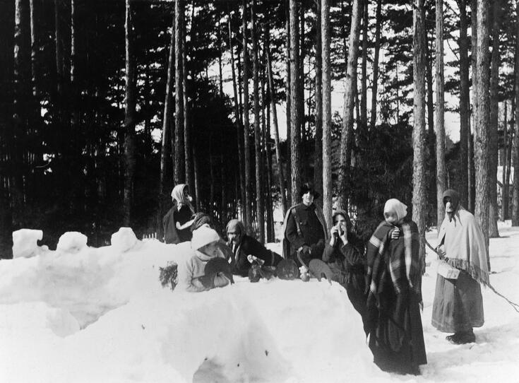 Nuoria pukeutuneina noidiksi lumilinnan vieressä, lumilinnan päällä paperisia pääsiäiskoristeita