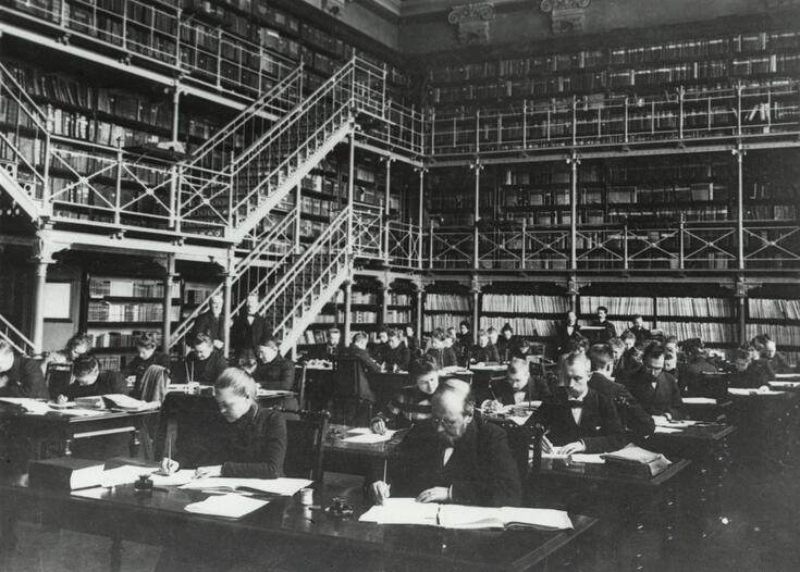 En grupp männiksor arbetar vid skrivborden i forskarsalen vars väggar är täckta med bokhyllor.