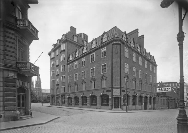 Kulmatalo Korkeavuorenkadun ja Pieni Robertinkadun risteyksessä, Korkeavuorenkatu 20 - Pieni Robertinkatu 10. Risteyksen kohdalla on sisäänkäynti Leijona-apteekkiin. Ylin ikkunarivi kuuluu katon puhkaiseville ullakkohuoneille. Rakennuksen oikealla puolella on kaksi matalaa puutaloa. Yrjönkadun vastaisen Pieni Robertinkatu 16:n rakennuksen tiiliseinässä on autokorjaamo Auto Company Oy:n mainos. Osa Johanneksen kirkkoa näkyy kulmatalon vasemmalla puolella. Katu on päällystetty katukivin. Valokuvan aivan oikea