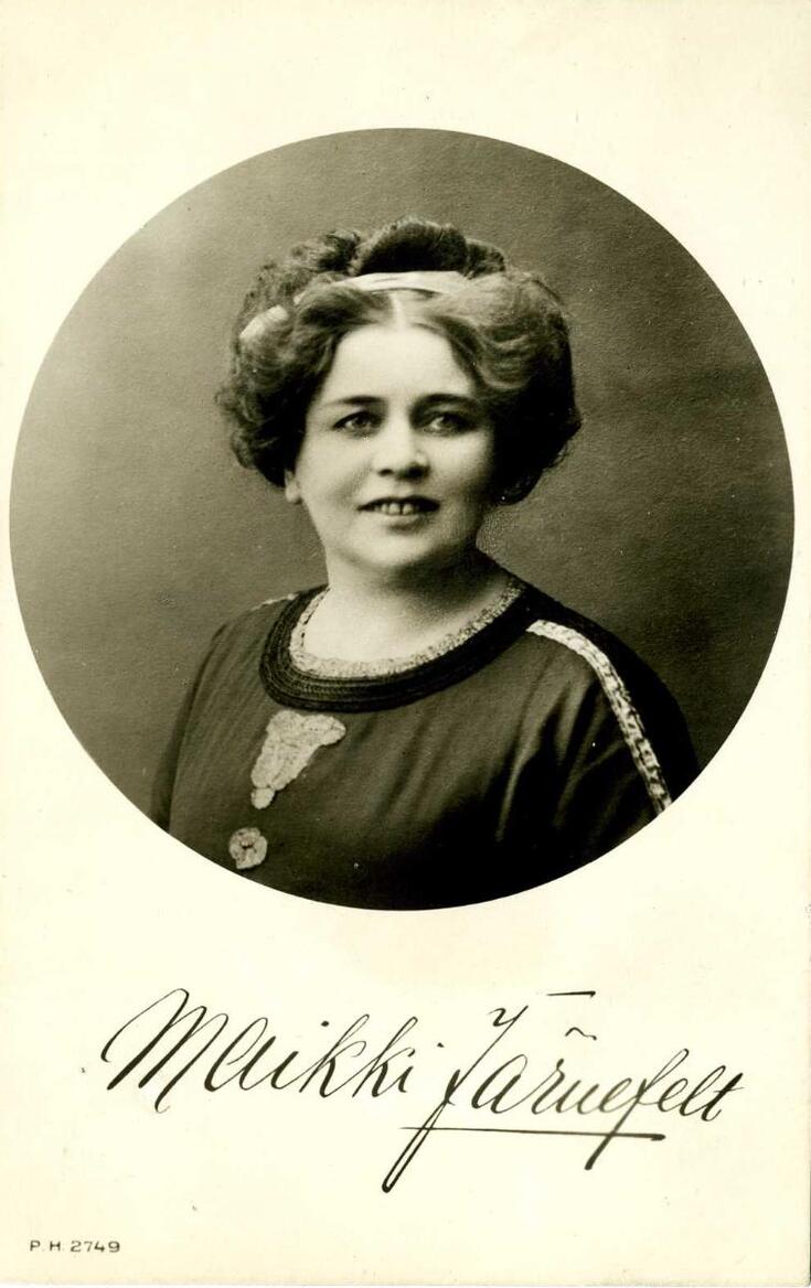 Bystfotografi av en leende mörkhårig kvinna med ett diadem i håret. Under fotografiet finns hennes namnteckning. 