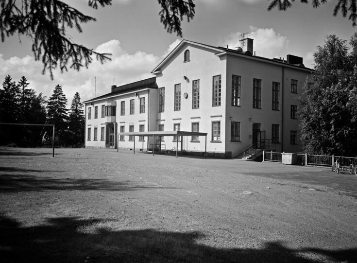 Puistolan vanha kansakoulu Puistolan vanha kansakoulu kuvattuna 6.8.1966. Rakennus toimi kouluna vuoteen 2015 asti. Jalmari Peltosen suunnittelema rakennus valmistui vuonna 1930. Rakennuksessa on toiminut myös sivukirjasto. Alt: Kaksikerroksinen valkoinen koulurakennus, jossa on harjakatto useista pienistä ruuduista koostuvat ikkunat. Pihamaalla ei näy ihmisiä. 