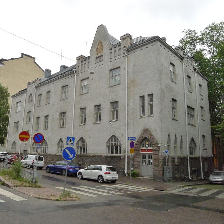 En gråputsad byggnad med parkerade bilar på gatan framför.