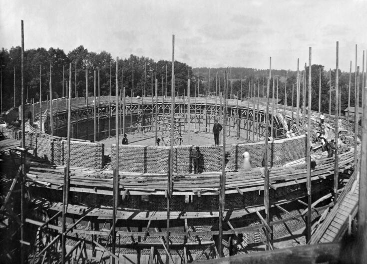 Kaasukellon rakennustyömaa. Tiilirakennuksen pyöreä runko on jo pystyssä kehikolla tuettuna, rakennusmiehiä seisoo telineillä.