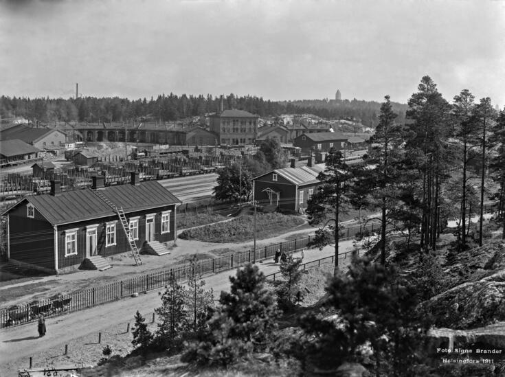 Foto från Västra Böle mot sydost och Böle bangård. På rälsen syns godsvagnar. I förgrunden små träbyggnader och bakom rälsen finns lokstallar.