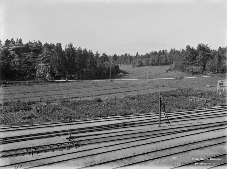 Näkymä länteen hieman Pasilan aseman pohjoispuolelta vuonna 1911. Nykyään täysin rakennetun ympäristön paikalla on peltoaukeaa ja metsiä.