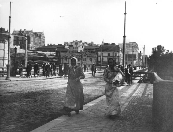 Kaksi huivipäistä työläisnaista kävelemässä Pitkälläsillalla kohti Siltasaarta.