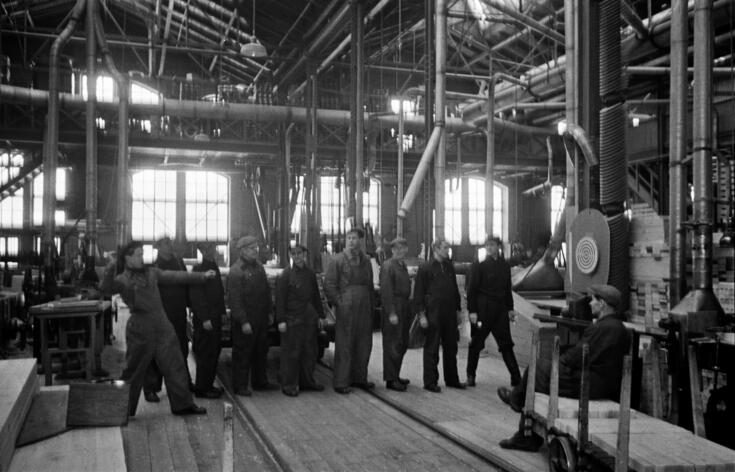 En grupp män i arbetsoveraller kastar pil på sin paus i Böles mekaniska verkstads hall.