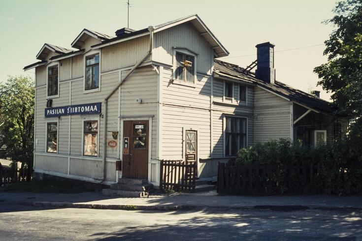 Affärsbyggnad av trä i gamla Trä-Böle, på väggen en skylt med texten ”Pasilan Siirtomaa”