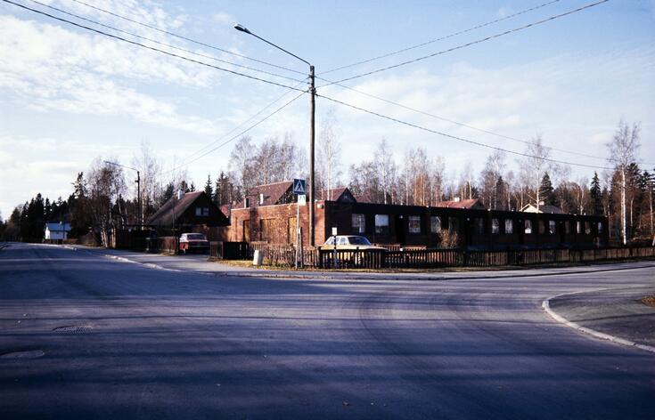 Radhus i rödtegel med plant tak, bakom dem syns egnahemshus med sadeltak.
