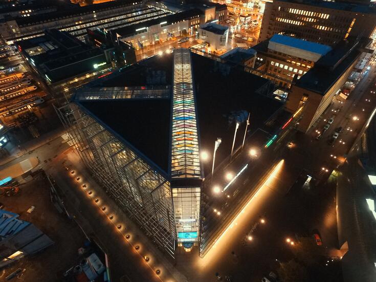 Flygfotografi av Sanomahuset kvällstid. Det centrala elementet i fotografiet är Sanomahusets takfönster. Baktill till vänster syns huvudjärnvägsstationen, till höger upptill Posthuset.