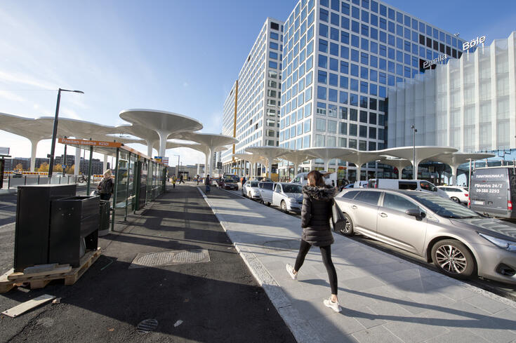 Vy mot Böle stationsplats. I förgrunden en busshållplats för en stomlinje, i bakgrunden höjer sig köpcentret Triplas höga byggnader.