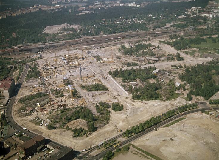 Ilmakuva Itä-Pasilasta. Muutaman rakennuksen runko on rakenteilla, muuten alue on hiekkapohjaa ja metsää.