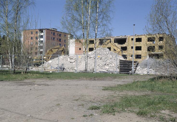 Alakiventien kerrostaloja puretaan Myllypurossa. Kuvassa osin purettu rakennus, jonka edessä on korkea rakennusjätekasa ja kaksi kaivuria.