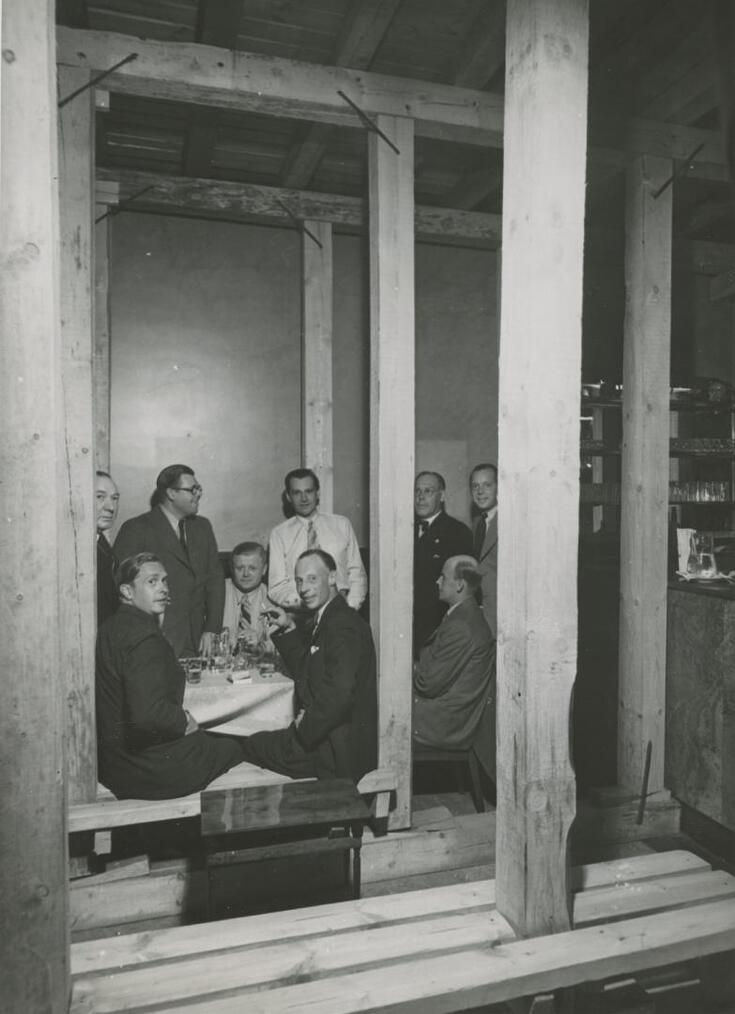 Män sitter vid ett bord i en bar, balkar stöder upp rummet.