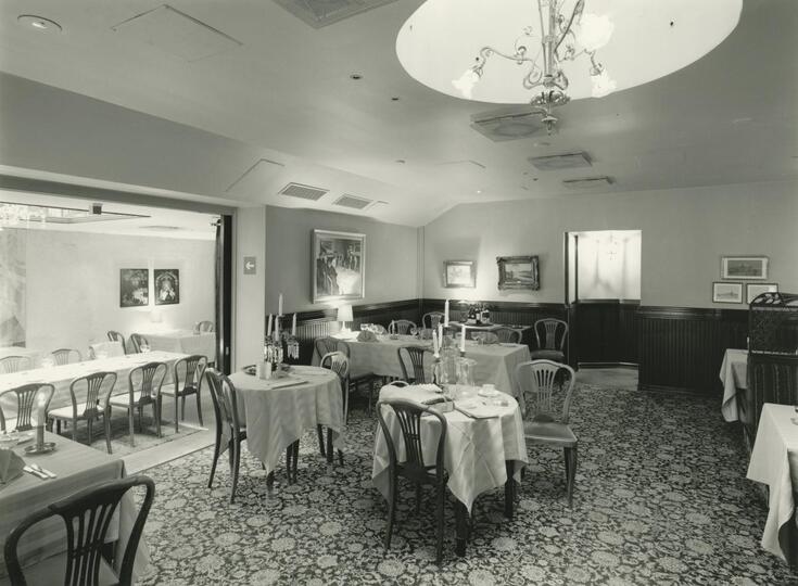 Restauranginteriör med dukade bord och dekorativ heltäckande matta. Till vänster syns en mindre sal.