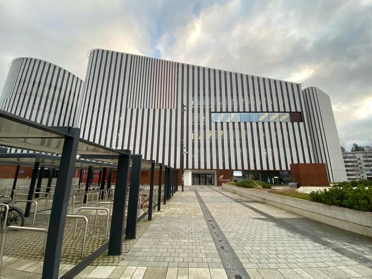 Vaalea kaarevan muotoinen julkisivu, etualalla pyöräkatos.