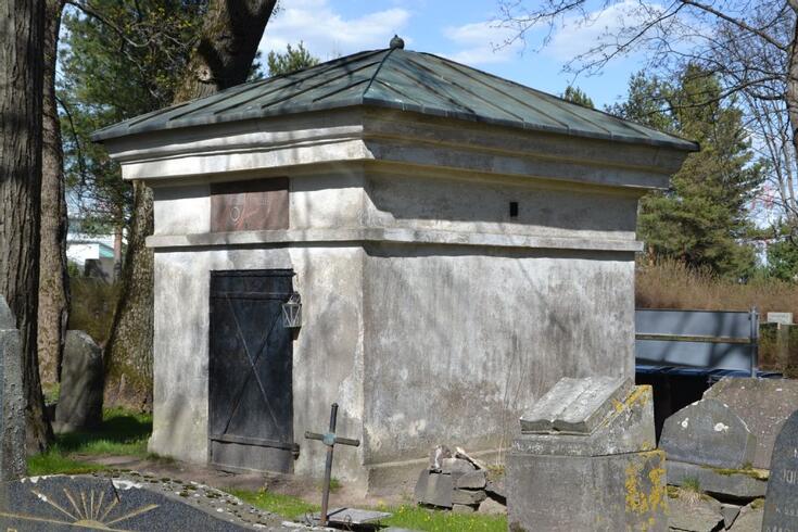 Valkoinen suorakaiteen muotoinen hautakappeli, jossa on aumakatto ja metalliovi.