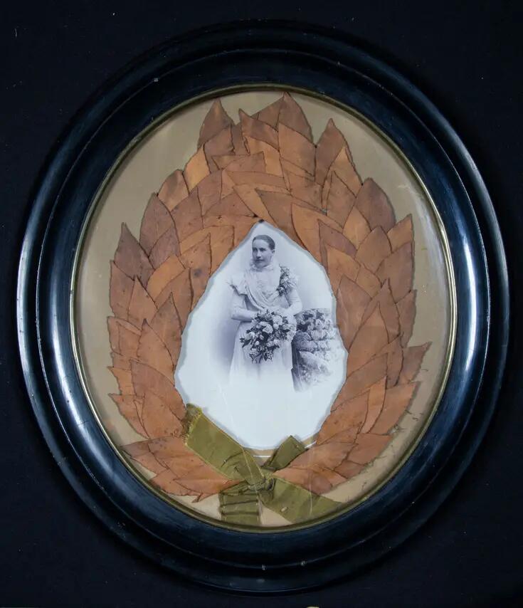 En lagerkrans som omges av en svart ram och har ett svartvitt fotografi av en ung kvinna i mitten