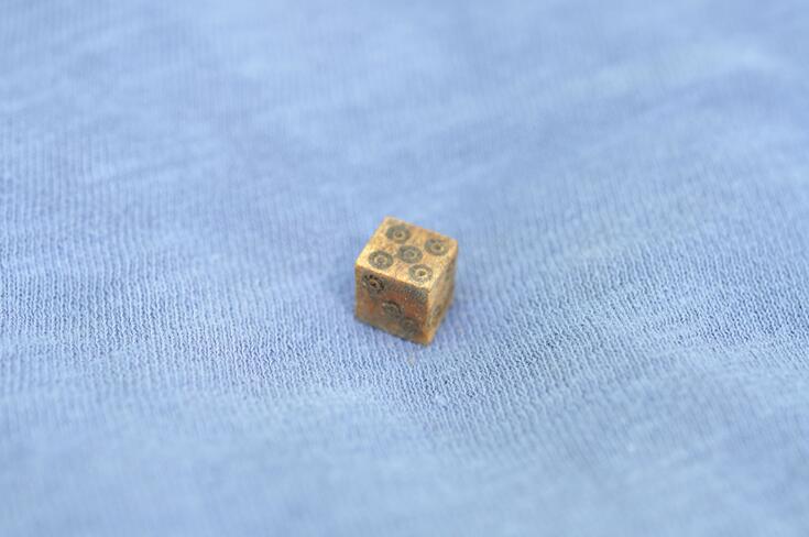 En liten tärning gjord av ben mot en bakgrund av ljusblått tyg