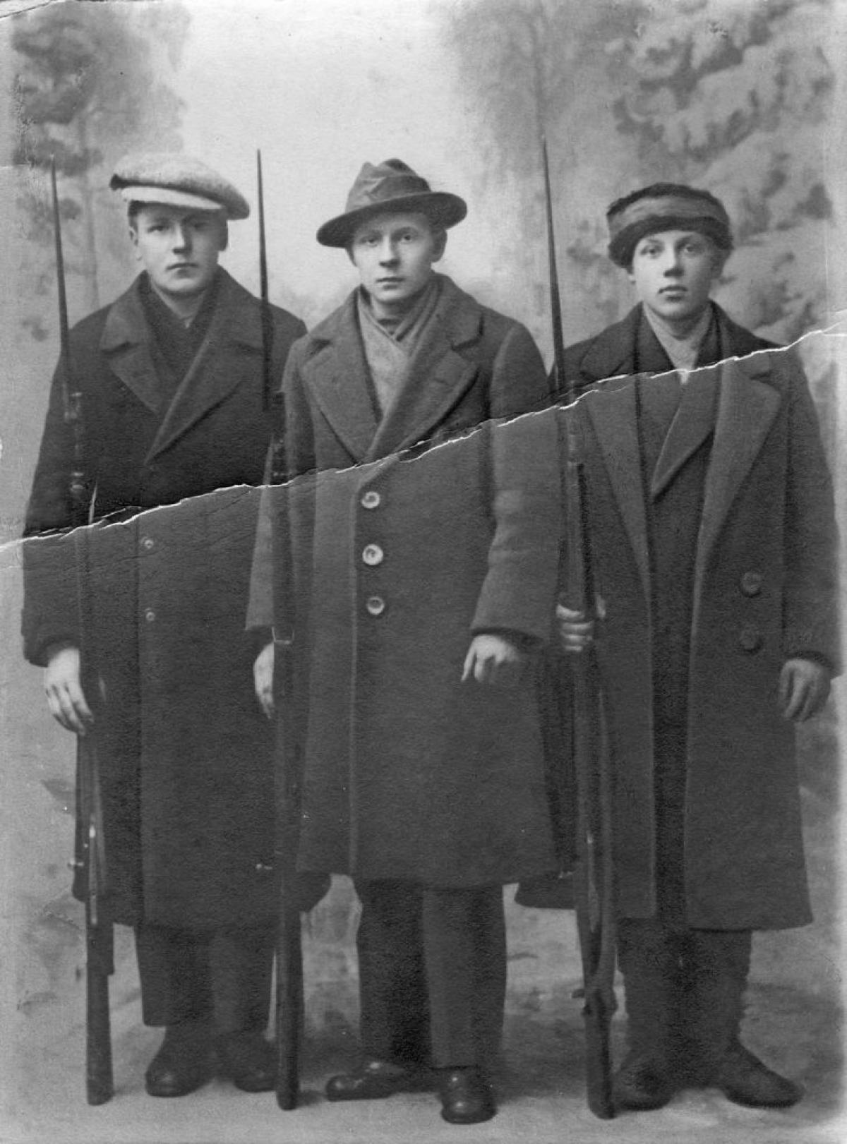 Kolme pitkiin takkeihin pukeutunutta punakaartilaista poseeraa muotokuvassa kiväärit käsissään.