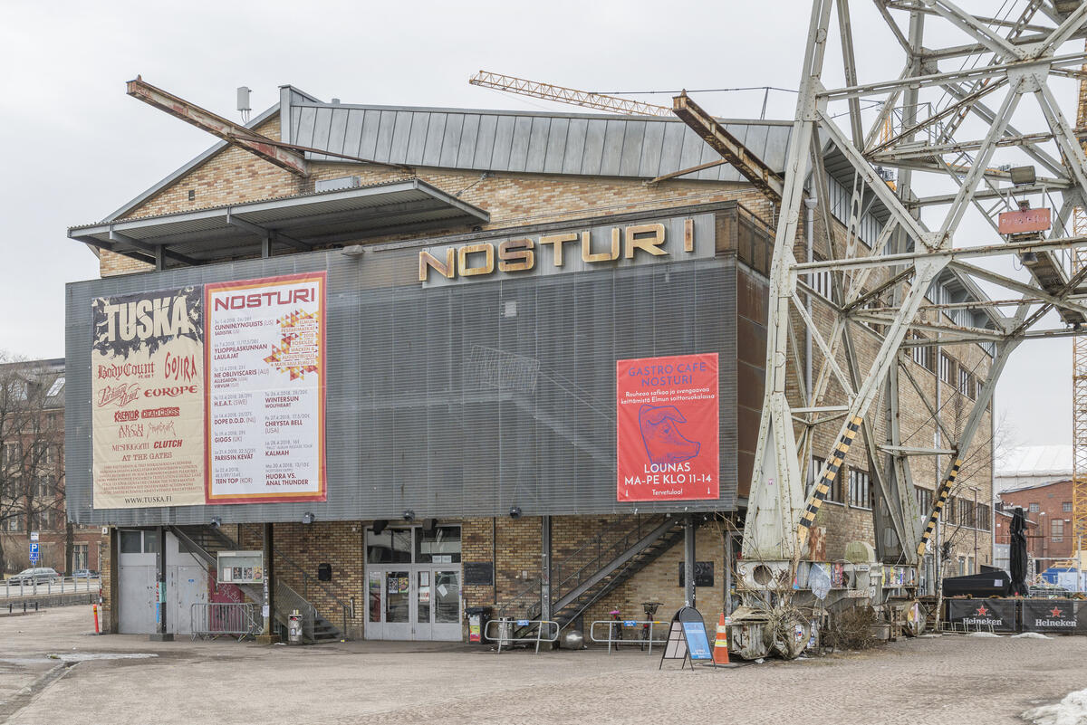 Vaaleankeltainentiilirakennus, jonka julkisivua peittävät isot keikkajulisteet ja metalliset portaat. Kuvan oikeassa reunassa näkyy ison nosturin alaosaa.