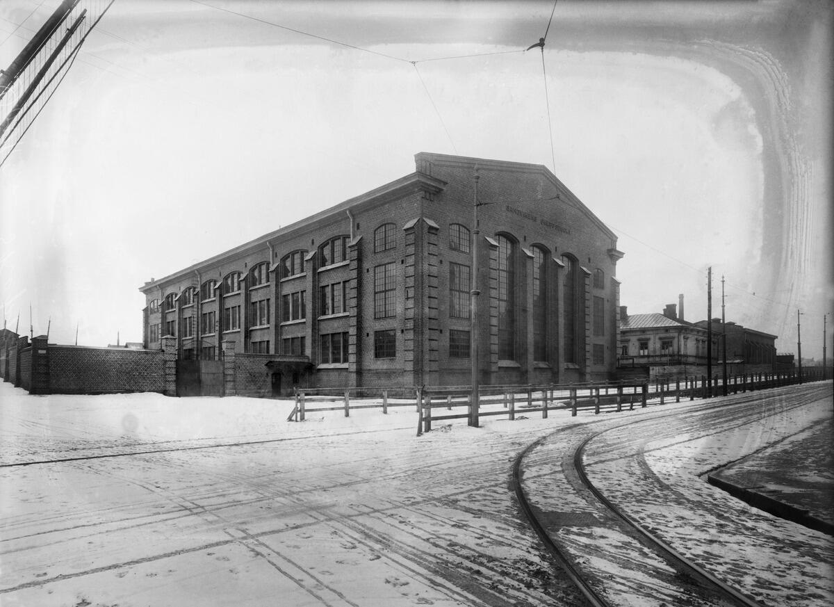 En fabriksbyggnad av tegel fotograferad på vintern. I förgrunden löper spårvagnsskenor.