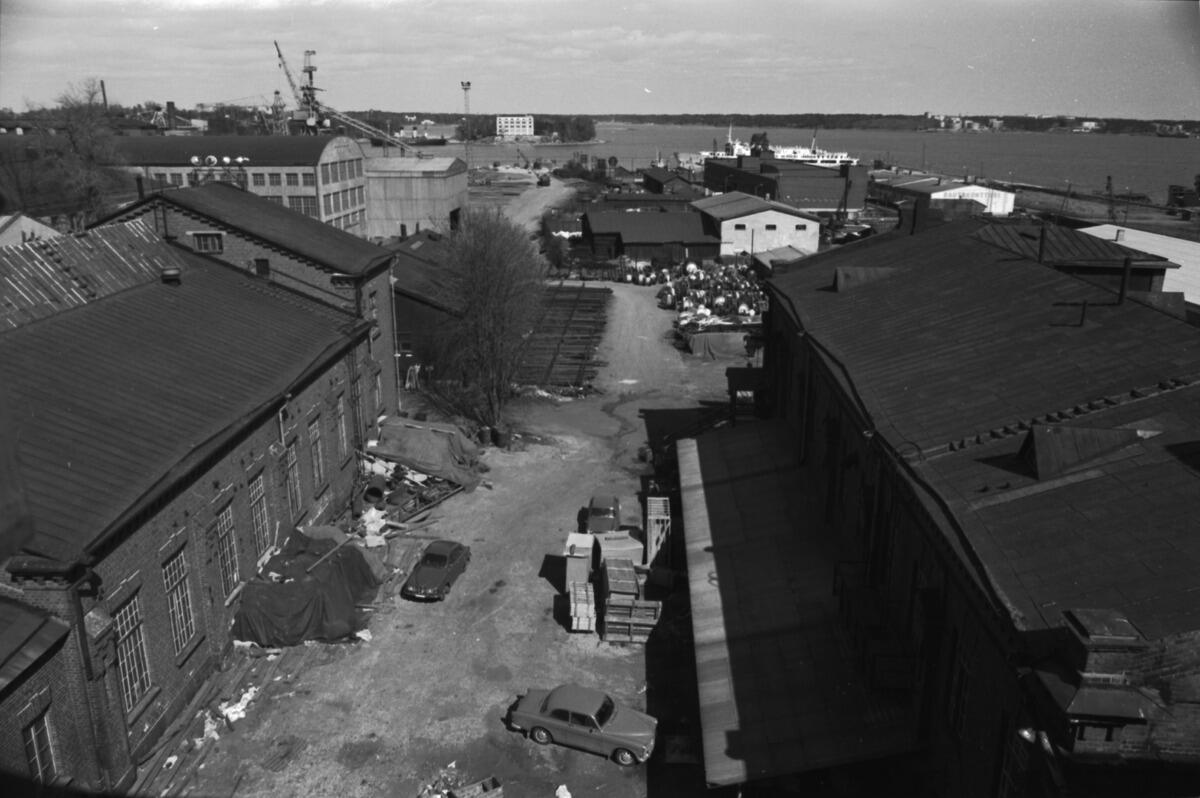 Amiralsgränden. Utsikt från Tolvskottsgatan från Lusborgens balkong mot nordost och Skatuddens spets. Gatan kantas av industri- och lagerbyggnader. I bakgrunden syns Vrakholmen, till höger Degerö.