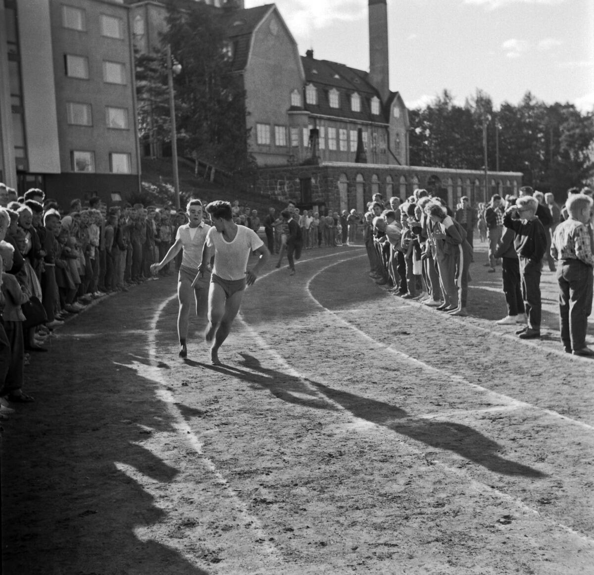 Juoksuradalla juoksee nuoria miehiä, ympärille on kokoontunut yleisöä.