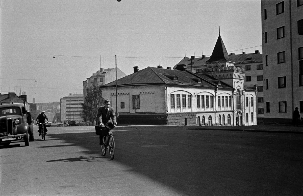 Katunäkymä Sturenkadulta, etulalla pyöräilijöitä ja auto. Taustalla Vapaaopisto Kalliola (Kalliolan työkeskus), Sturenkatu 11 - Kalliolanrinne 5.