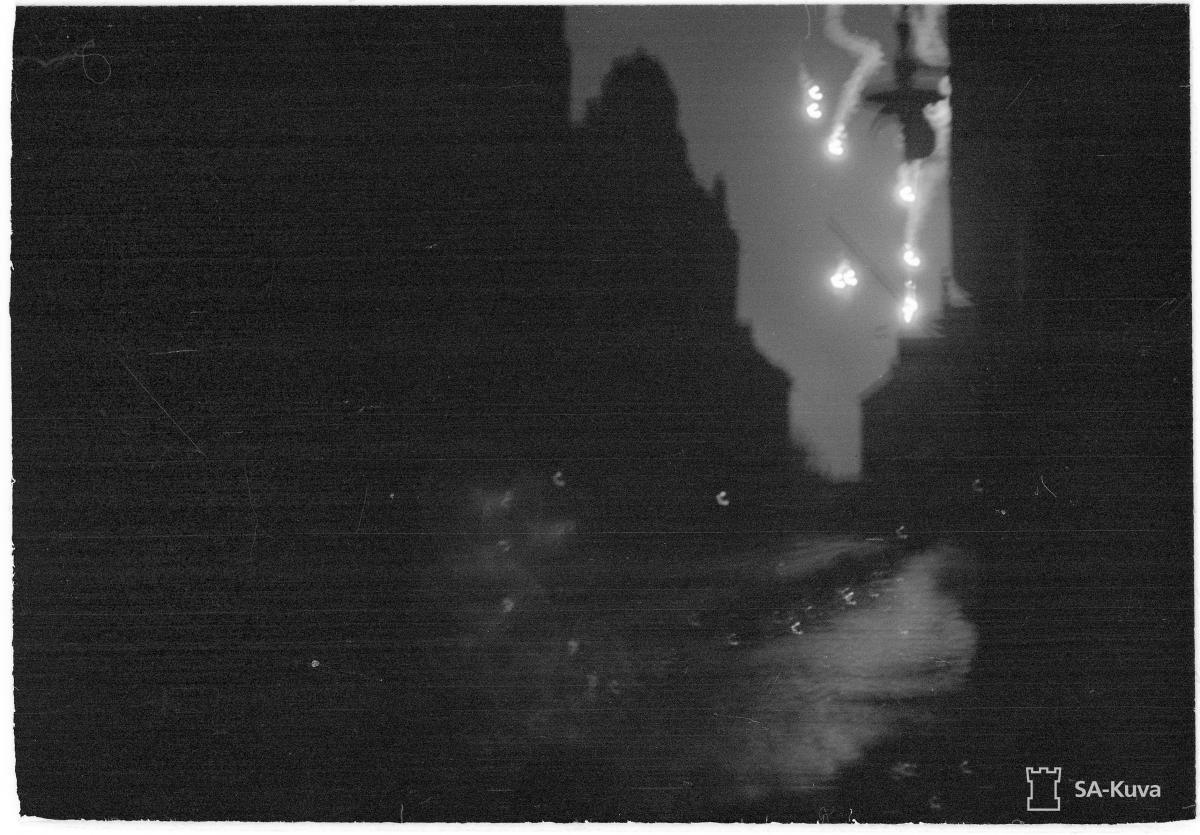 Valopommeja Tehtaankadun yllä 6.2.1944, vasemmalla Tehtaankatu 5. Ennen pommien pudottamista viholliskoneet pudottivat valopommeja valaistakseen täysin pimeän kaupungin kohteet. Kaupungissa valitsi sota-aikana pimennysmääräys, jonka rikkomisesta rangaistiin. Kuvaaja: Leo Vepsäläinen / SA-kuva