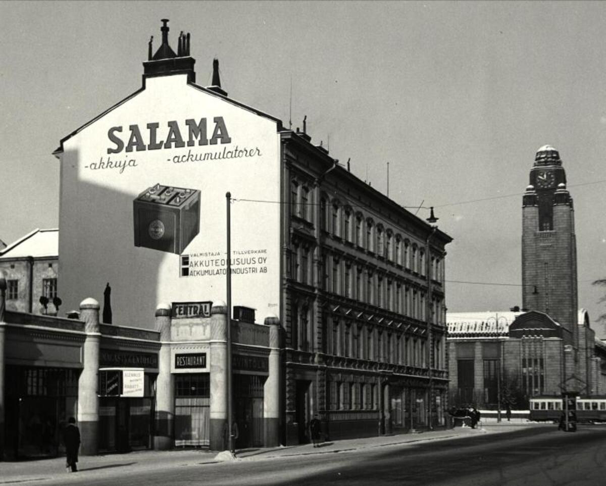 Till vänster det låga huset med restaurang Central, i mitten Skohahuset i hörnet av Brunnsgatan och Centralgatan. Till höger syns järnvägsstationens klocktorn. Skohahuset revs 1965, och 1967 byggdes på stället City Center, alltså Korvhuset.