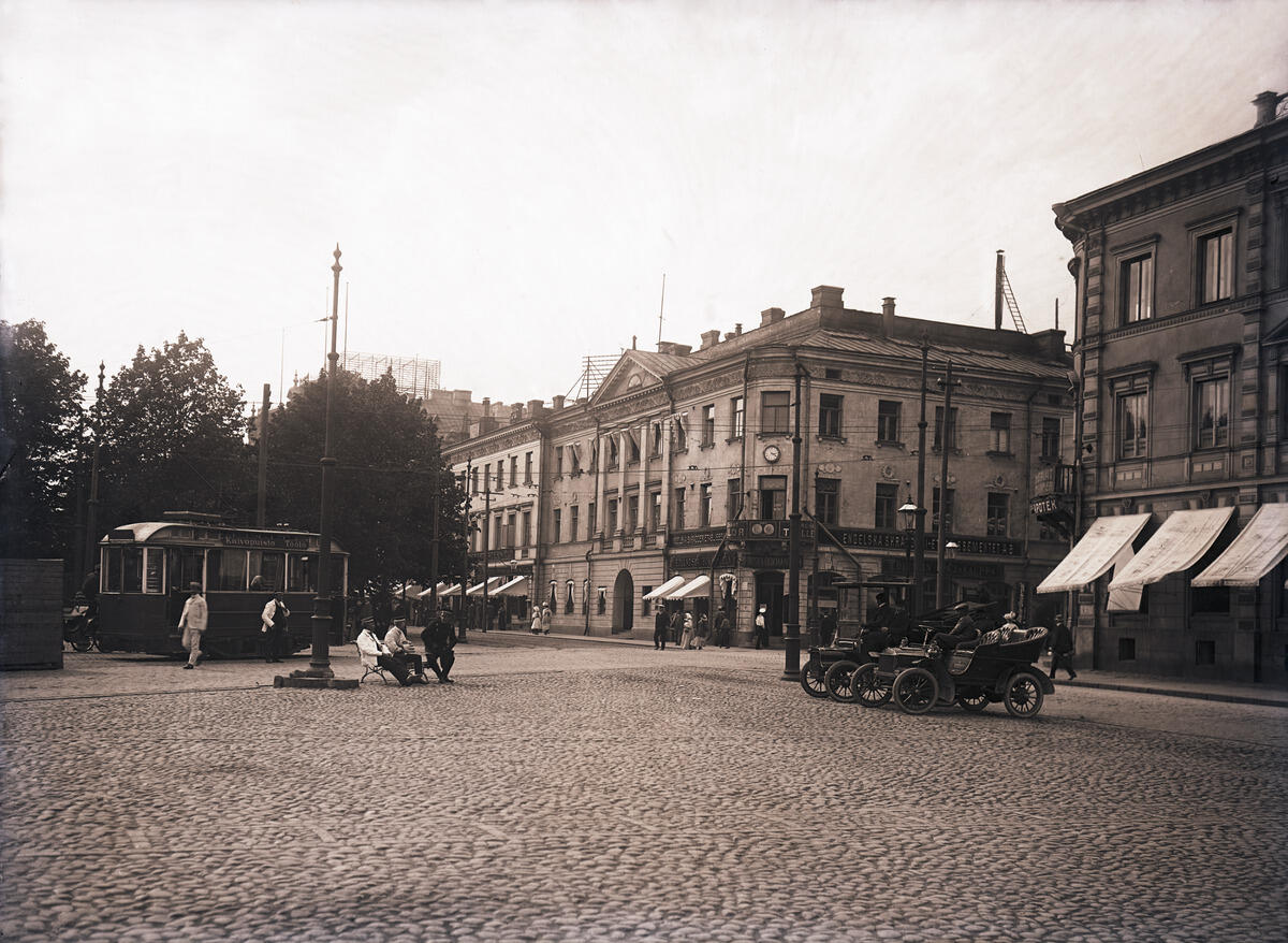 Helsingin ensimmäinen vuokra-autoasema kauppatorin laidalla, Pohjoisesplanadi 19, 21. Edessä Oldsmobile, vieressä osittain katettu Cadillac, molemmat vm 1905. Ensimmäinen taksilupa annettiin 1906.