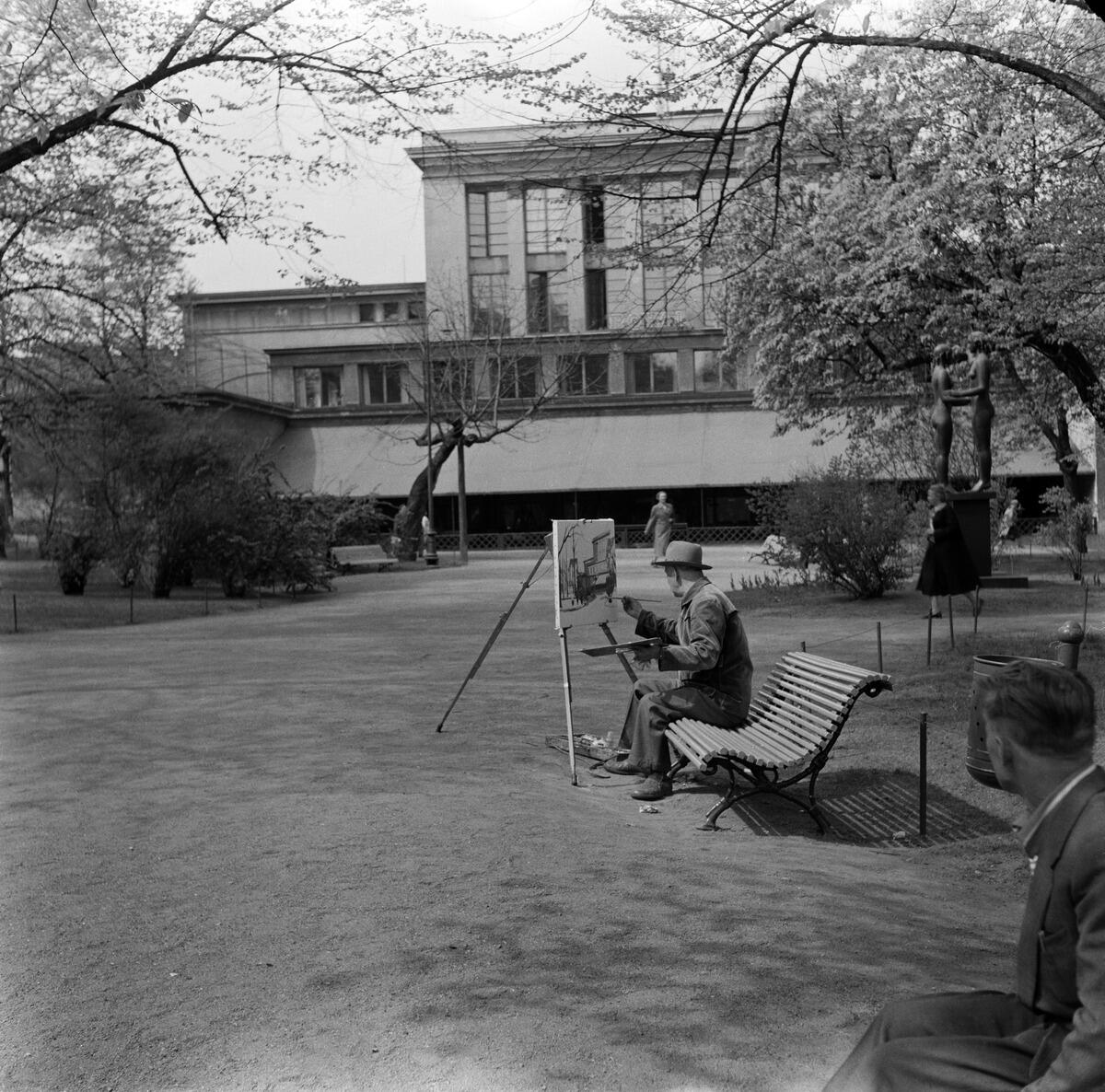 Esplanadparken, Teateresplanaden, en målare arbetar på en parkbänk. I bakgrunden ses Svenska teatern och restaurang Royal, till höger Gunnar Finnes skulptur Saga och sanning (1932).