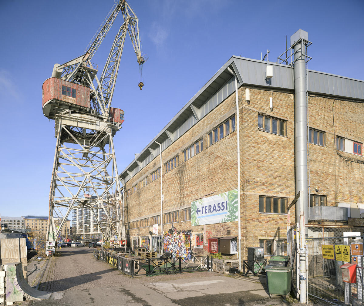 •	Kultur- och allaktivitetshuset Nosturi sett från havsstranden. I Nosturi arrangerades spelningar och andra evenemang, och dessutom fanns Elmus kontorslokaler, restaurangverksamhet och replokaler för band i huset. Längst fram till höger syns skyltar på ett nätstängsel med information om byggarbetsplatsen invid Nosturi.