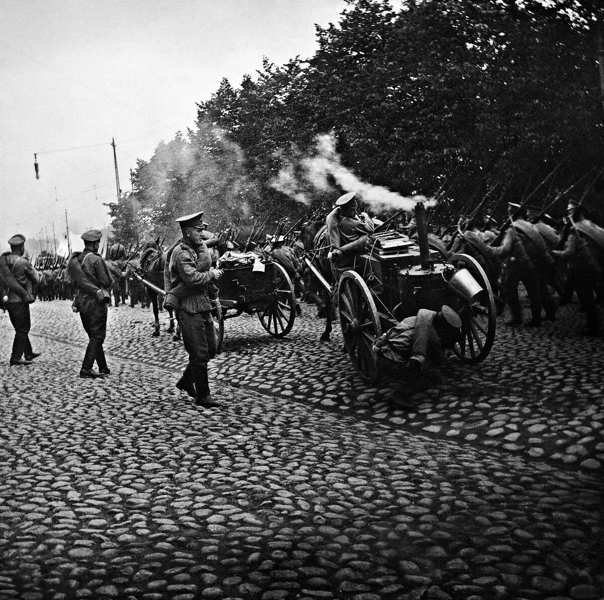 Sotilasosasto marssii Helsingissä kiväärit olallaan. Kuvan etualalla sotilaat tarkastelevat hevosen vetämää kenttäkeittiötä.
