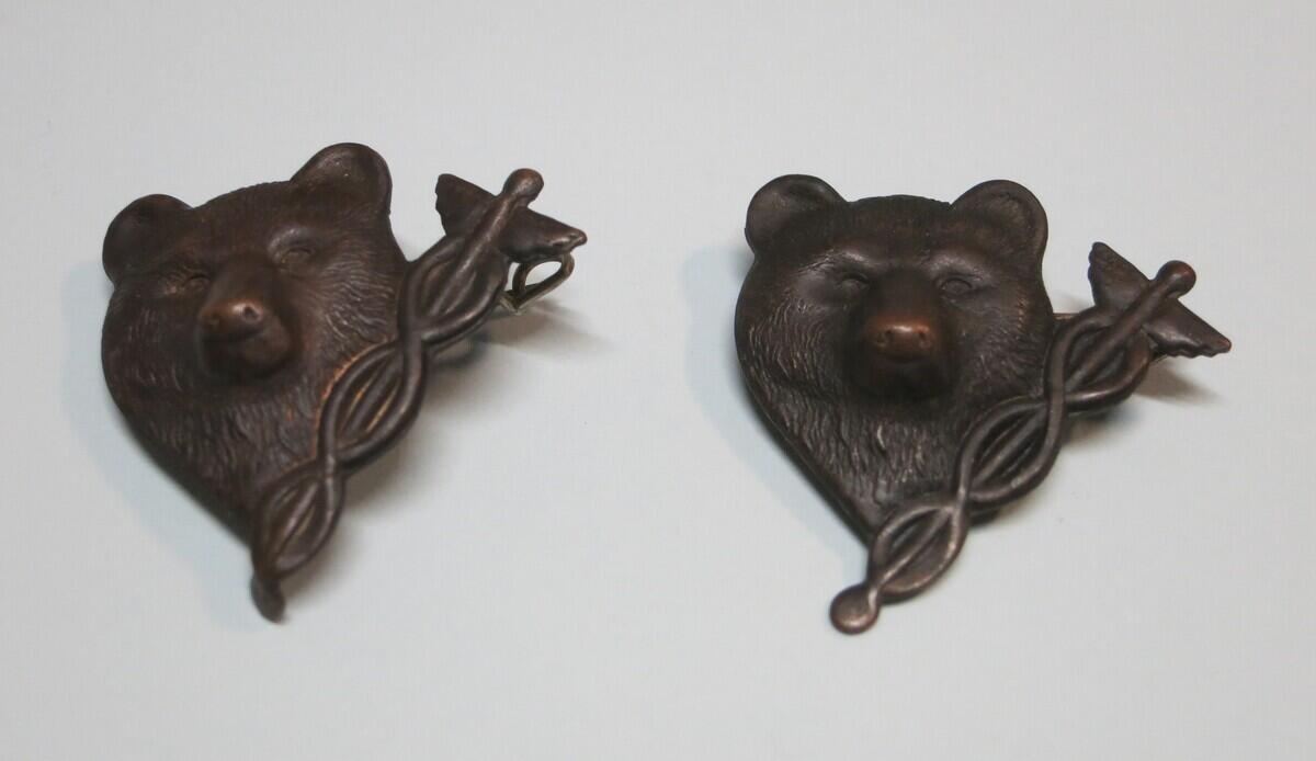 Två likadana rockmärken i patinerad metall föreställande ett björnhuvud med en hermesstav.