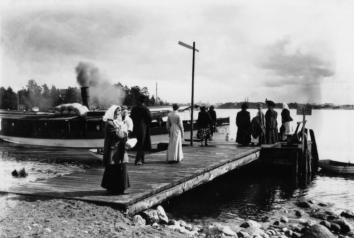 Passagerare väntar på att gå ombord på ångbåten Svea vid Smedjevikens brygga på Drumsö på 1910-talet. Ångfartyget Svea står vid bryggan.