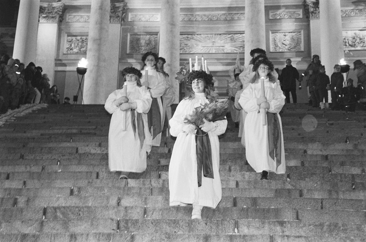 En ung kvinna med vita kläder och en krona med ljus skrider ner för Helsingfors domkyrkas trappor 