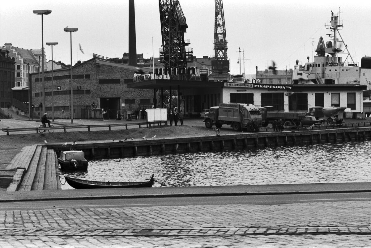 Utsikt från Sandvikskajen 13 mot sydost. I förgrunden syns Sandvikens hamnbassäng och två utombordare. Till vänster, i utkanten av Oy Wärtsilä Ab:s varvsområde, syns en lagerbyggnad (sedermera kultur- och allaktivitetshuset Nosturi), till höger Unions bensinstation, och bakom den isbrytaren Murtaja. Wärtsiläs varv i bakgrunden.