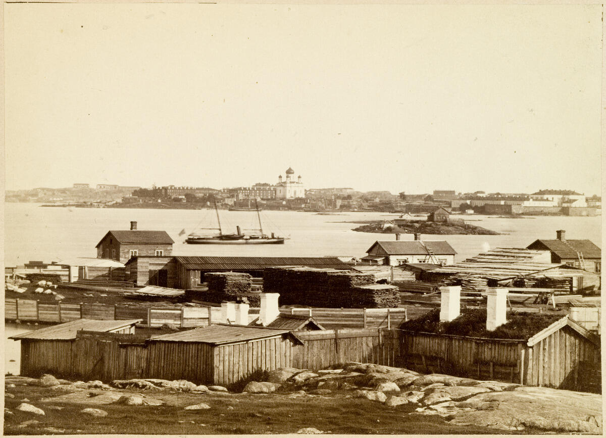 A view of southeastern Katajanokka, merchant Ekebom's ferry yard on Lökholmen, or Laukkasaari Island. Iso Mustasaari of Sveaborg (Suomenlinna) in the background. Suomenlinna Church housed an Orthodox congregation at the time, as evidenced by the domes.