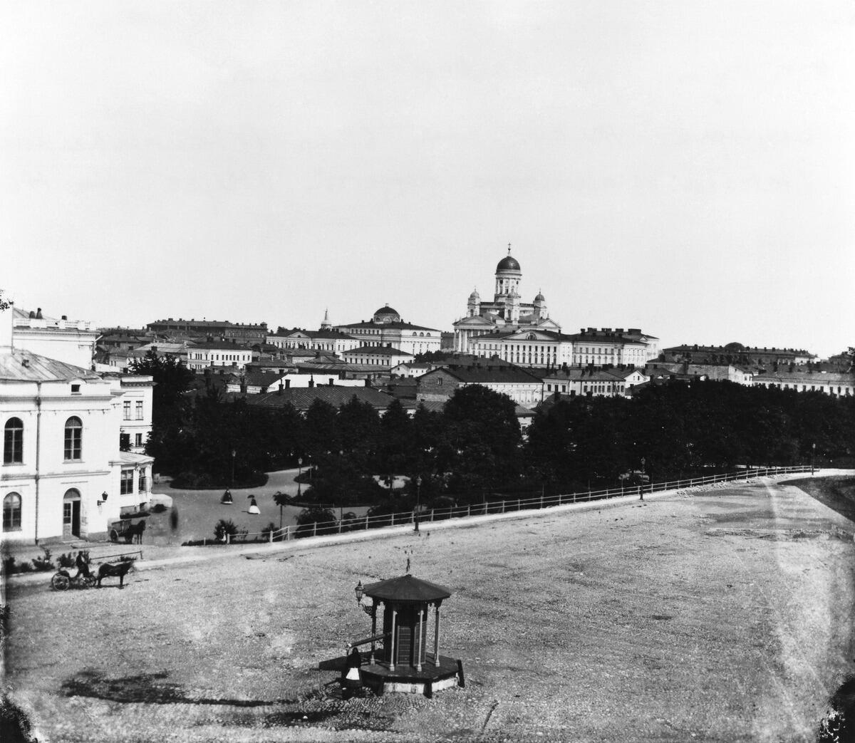 Keskellä Erottajan kaivo. Taustalla Nya Teatern ja Teatteriesplanadi. Erottajan kaivo muutettiin kuvassa näkyvään muotoon 1869. Nähtynä Heikinkatu 6:sta (Mannerheimintie 2:sta), jossa sijaitsi valokuvaaja E. Hoffersin ateljee vsta  1867.