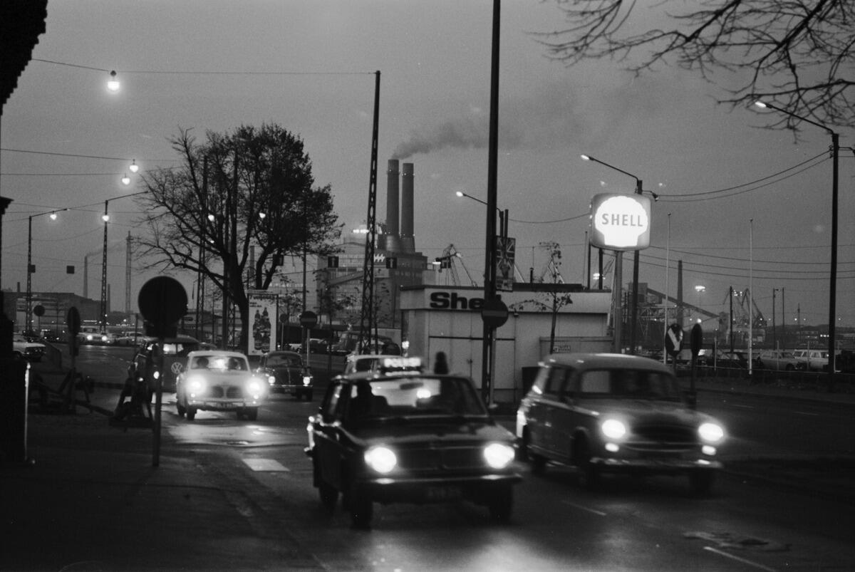 Kruununhaka, Pohjoisranta. Vehicular traffic at dusk in Pohjoisranta at the corner of Maneesikatu. There is a Shell service station in the middle of the picture, and Hanasaari A Power Plant can be seen in the background.