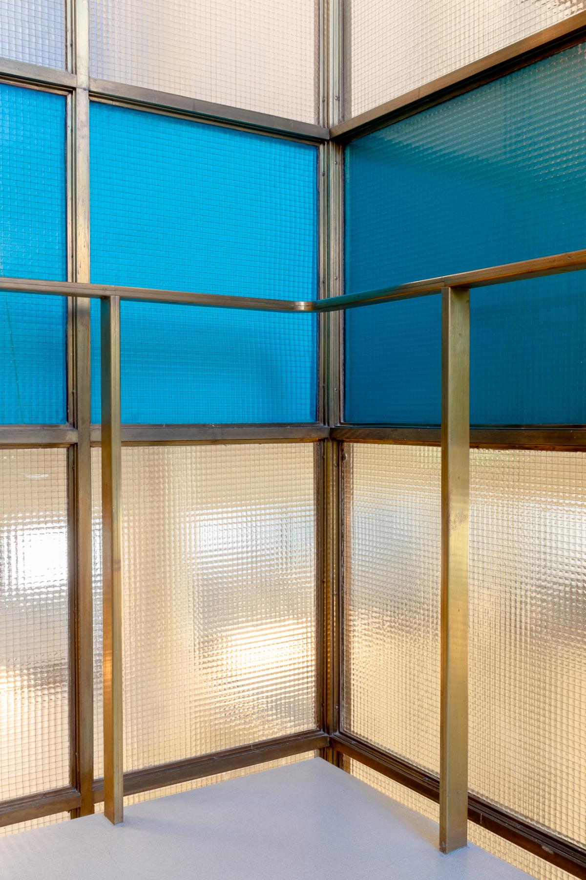 Kuva osittain sinisestä, osittain värittömästä lasiseinästä jossa rusehtavat metallireunukset
