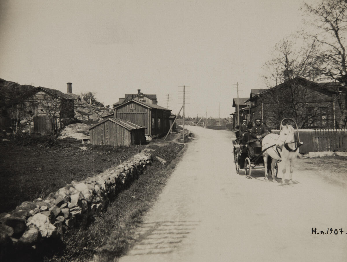 Östra Chaussén (numera Tavastvägen) vid de södra delarna av Gamla stan (nuvarande Gammelstaden). Till höger i bakgrunden nuvarande Forsparkens område. Helsingfors Fornminnesnämnd och fotografen Signe Brander på "söndagsutflykt" för att inspektera fotograferingsställen i Gammelstaden på Östra Chaussén (Tavastvägen 166, 165).