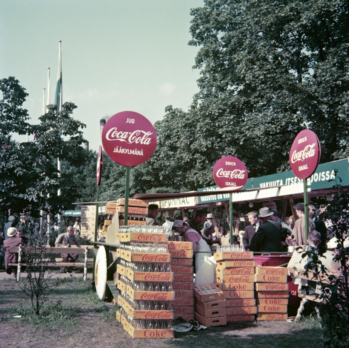 Coca-Colan myyntipiste Hesperian puistossa. Pullokorit täyttävät myyntipisteen edustan, johon on kerääntynyt jonoa.