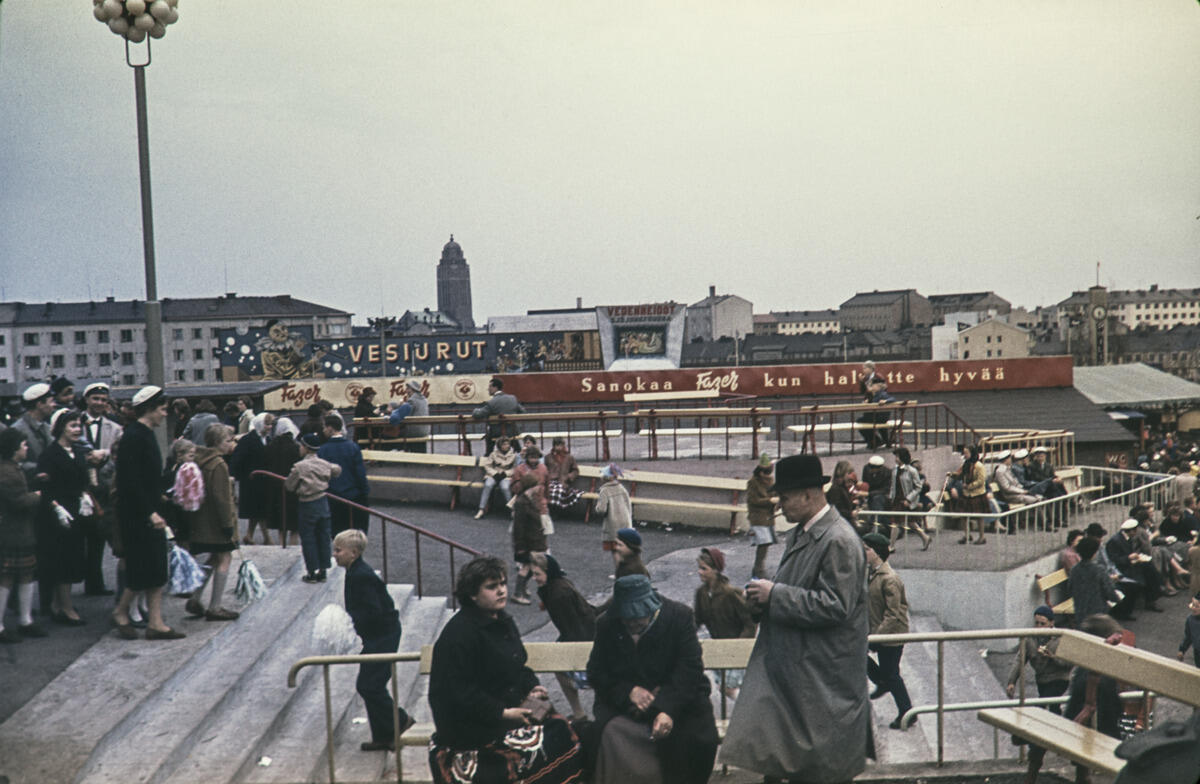 Människor på Borgbacken med studentmössor och förstamajviskor. I bakgrunden syns Fazers reklam.