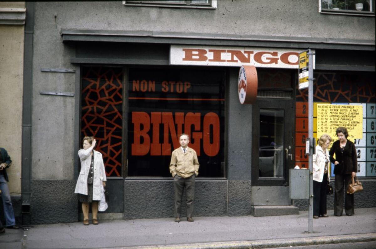 ihmisiä seisoo non stop bingo -liikkeen edessä bussipysäkillä