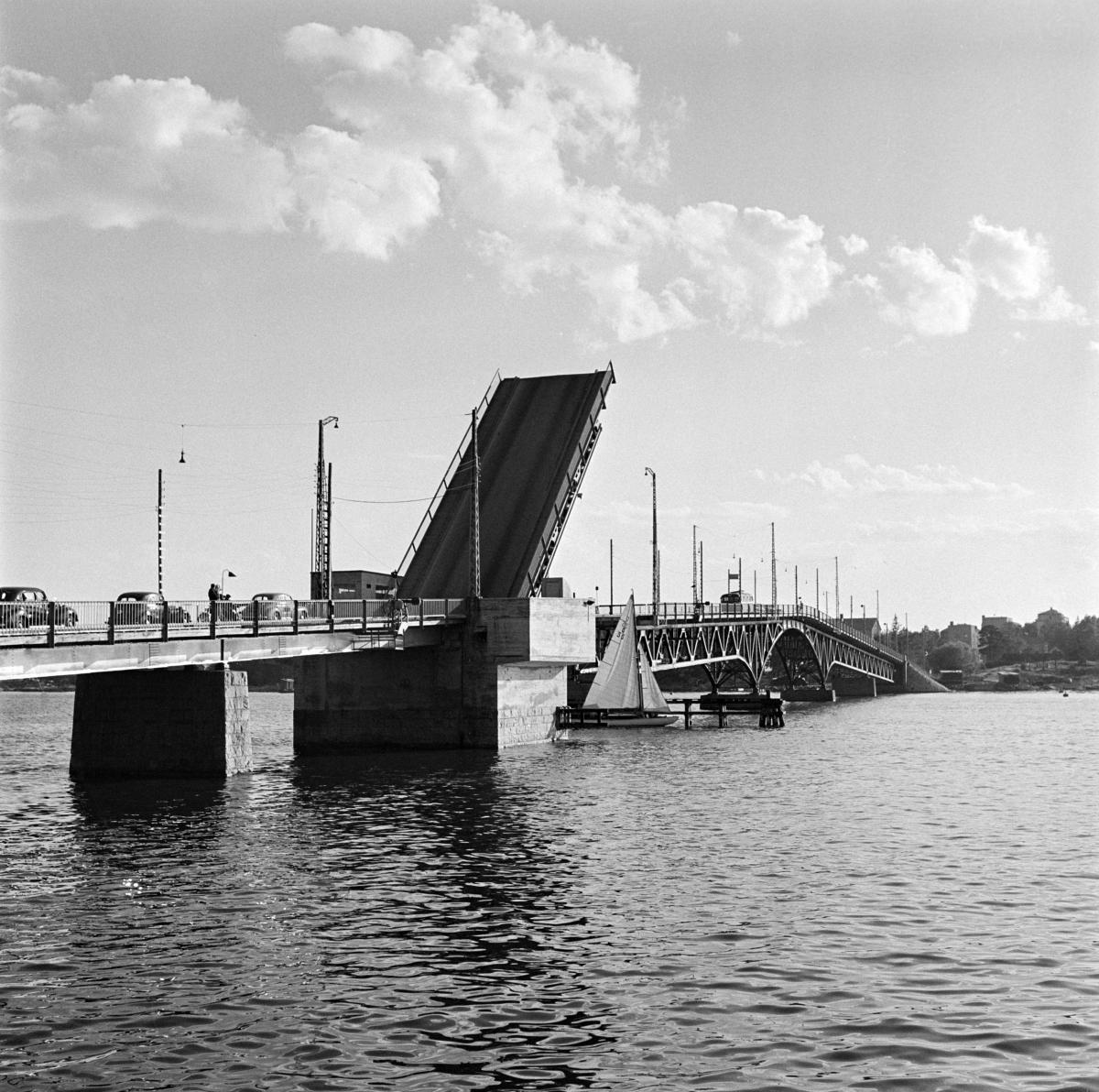Den första bron till Drumsö. Bilden tagen år 1953 från Sundholmen. Klaffbron har fällts upp och bilar står i kö i väntan på att få köra över bron. Ett litet segelfartyg passerar under bron. 